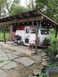 an rv is parked under a covered area with chairs and flowers on the porch next to it