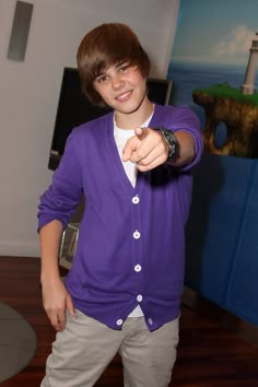 a young man pointing at the camera while wearing a purple cardigan