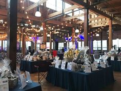 an indoor event with tables covered in blue cloths and lights hanging from the ceiling