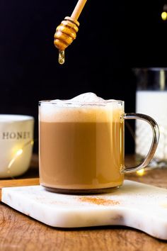 a glass mug filled with liquid sitting on top of a table next to a spoon