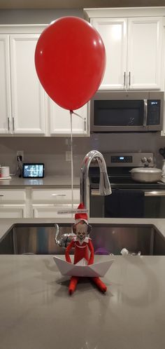 an elf is holding a red balloon above a sink in the middle of a kitchen