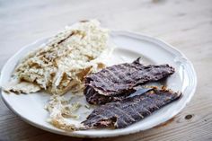 a white plate topped with meat and mashed potatoes on top of a wooden table