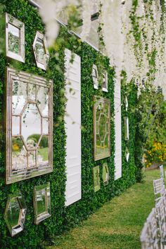 an outdoor wedding ceremony with white chairs and greenery on the wall, decorated with mirrors