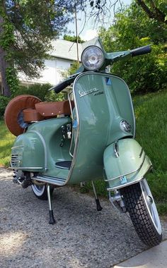 a green scooter parked on the side of a road next to grass and trees