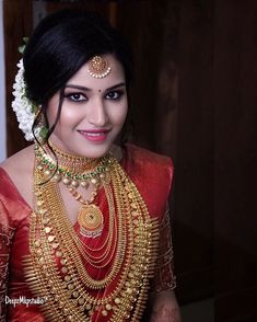 a woman in a red and gold sari with jewelry on her neck, smiling at the camera