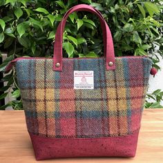 a multicolored plaid bag sitting on top of a wooden table next to a bush