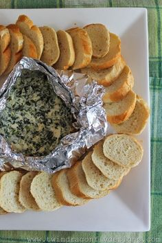 a white plate topped with bread slices and a bowl of blue cheese dip surrounded by crackers