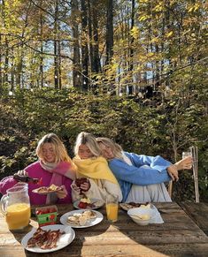 three women sitting at a picnic table with food and drinks in front of their faces