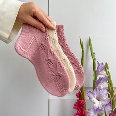 a person holding a pair of pink socks in front of purple and white flower arrangement