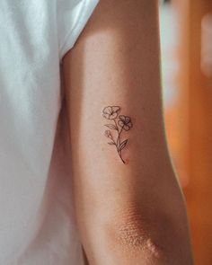 a woman's arm with a small flower tattoo on the left side of her arm