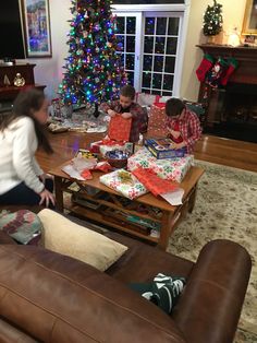 a group of people sitting around a living room with christmas presents on the couches