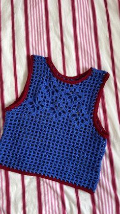 a blue crocheted top laying on a striped bed sheet with red and white stripes