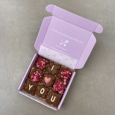 a purple box filled with lots of chocolates on top of a cement floor covered in sprinkles