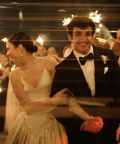 a man and woman standing next to each other in front of people holding sparklers