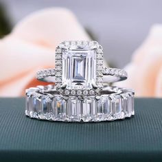 an emerald cut diamond ring and matching wedding band on top of a green box with roses in the background