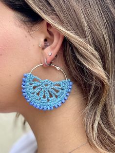 a close up of a woman's ear wearing large blue earrings with crocheted details