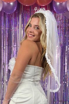 a woman in a wedding dress and veil posing for the camera with balloons behind her