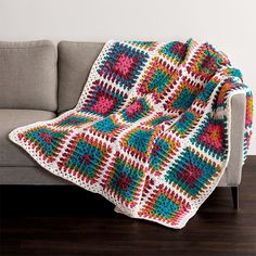 a crocheted granny blanket sitting on top of a couch next to a pillow