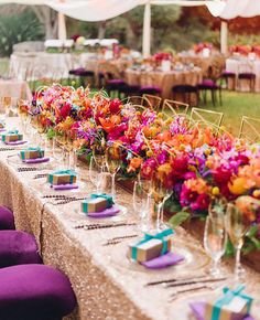 a long table with purple chairs and colorful flowers on the tables is set up for an event