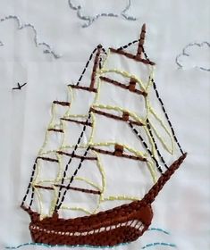 a sailboat made out of chocolate and white thread on a piece of paper with clouds in the background