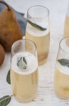 three glasses filled with liquid next to pears