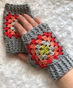 a hand is holding onto a crocheted gray and orange mitt on a white surface