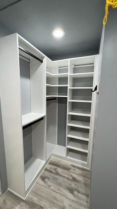 an empty walk in closet with white shelving and gray shelves on the wall, next to wooden flooring