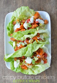 a white plate topped with lettuce covered in chicken wrappers on top of a wooden table