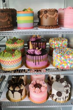 many different cakes are on shelves in a display case with frosting and sprinkles