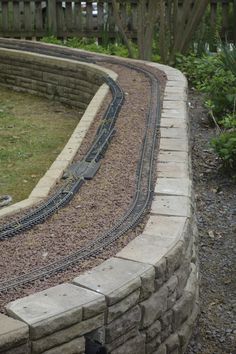 a toy train is going around the corner of a brick wall in a garden area