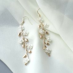 "Gold Floral Wedding earrings Gold Flower Bridal earrings Chandelier Wedding earrings Chandelier Bridal jewelry Gold Wedding jewelry These gentle bridal earrings are truly stunning and would add a romantic touch to any brides ensemble! Made from handcrafted clay flowers, 24K gold plated brass leaves they glisten and catch the light beautifully, whilst remaining classy, chic and understated. These earrings are extremely romantic! Description: - 24K Gold Plated Brass leaves - Handcrafted clay flow Floral Earrings Wedding, Flower Wedding Earrings, Bridal Gold Earrings Weddings, Gold Pearl Flower Earrings For Wedding, Silver Danglers For Wedding, Delicate Pearl White Flower Earrings For Wedding, Gold Dangle Flower Earrings For Wedding, Gold Bridal Drop Earrings With Flower Decoration, White Pearl Danglers For Wedding