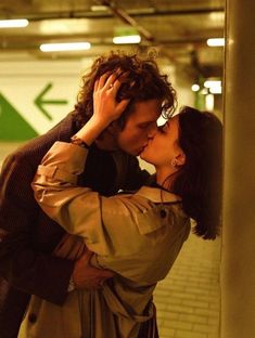 a man and woman kissing each other in a subway station with an arrow painted on the wall behind them