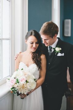 a bride and groom standing next to each other in front of a window with blue walls