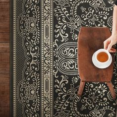 a person holding a cup of coffee on top of a wooden table next to a black and white wall