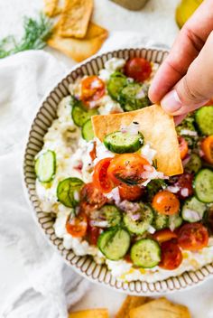 a person dipping a tortilla chip into a bowl of vegetables