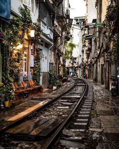 a train track running through an alleyway with buildings on both sides and people sitting at the end