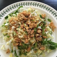 a salad with nuts and lettuce on a white plate sitting on a table