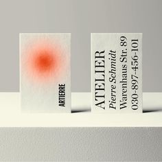 two business cards sitting on top of a white surface with an orange dot in the middle