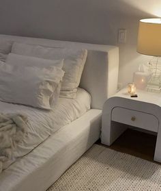 a white bed sitting next to a night stand with a lamp on top of it