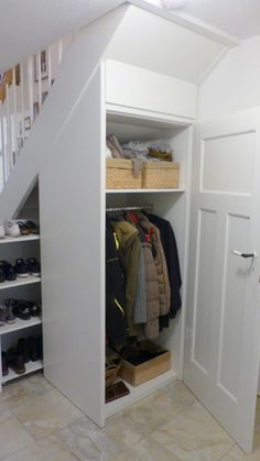 an open closet with clothes and shoes on the bottom shelf in front of a stair case