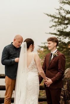 a bride and groom standing next to each other in front of a wooden fence holding hands