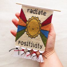 a hand holding a small cross stitch book with tassels on it's sides