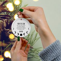 a person holding a christmas ornament in front of a pine tree with lights