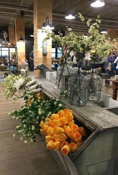 vases filled with flowers sitting on top of a wooden table in a room full of people