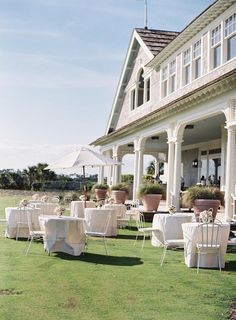 tables and chairs are set up in front of a large house with white linens