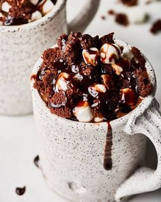 two mugs filled with hot chocolate and marshmallows on a white table