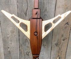 a wooden wall mounted clock with two pendulums on it's sides and an arrow shaped face