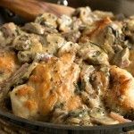 a pan filled with chicken and mushrooms on top of a wooden table next to bread