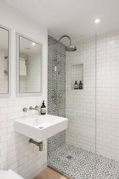 a white bathroom with black and white tile on the floor, shower stall and sink