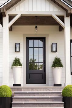 the front door of a white house with two planters on each side and steps leading up to it